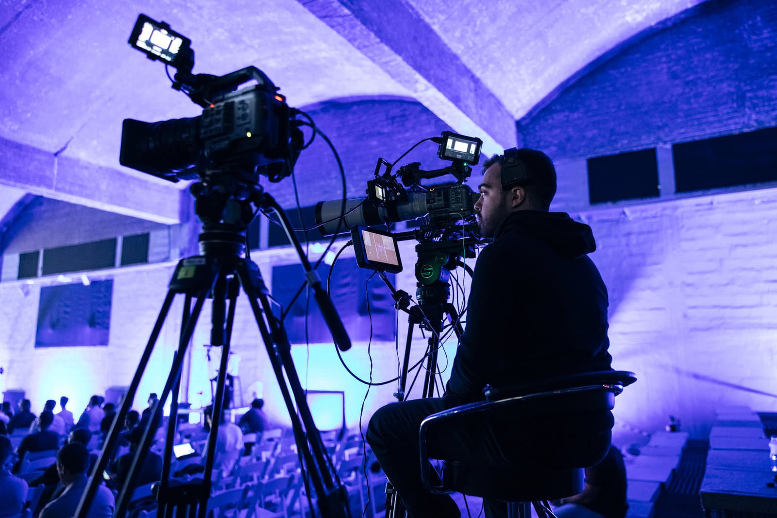 A Backlight operator in silhouette behind a live multi-camera rig, backlit by stage wash