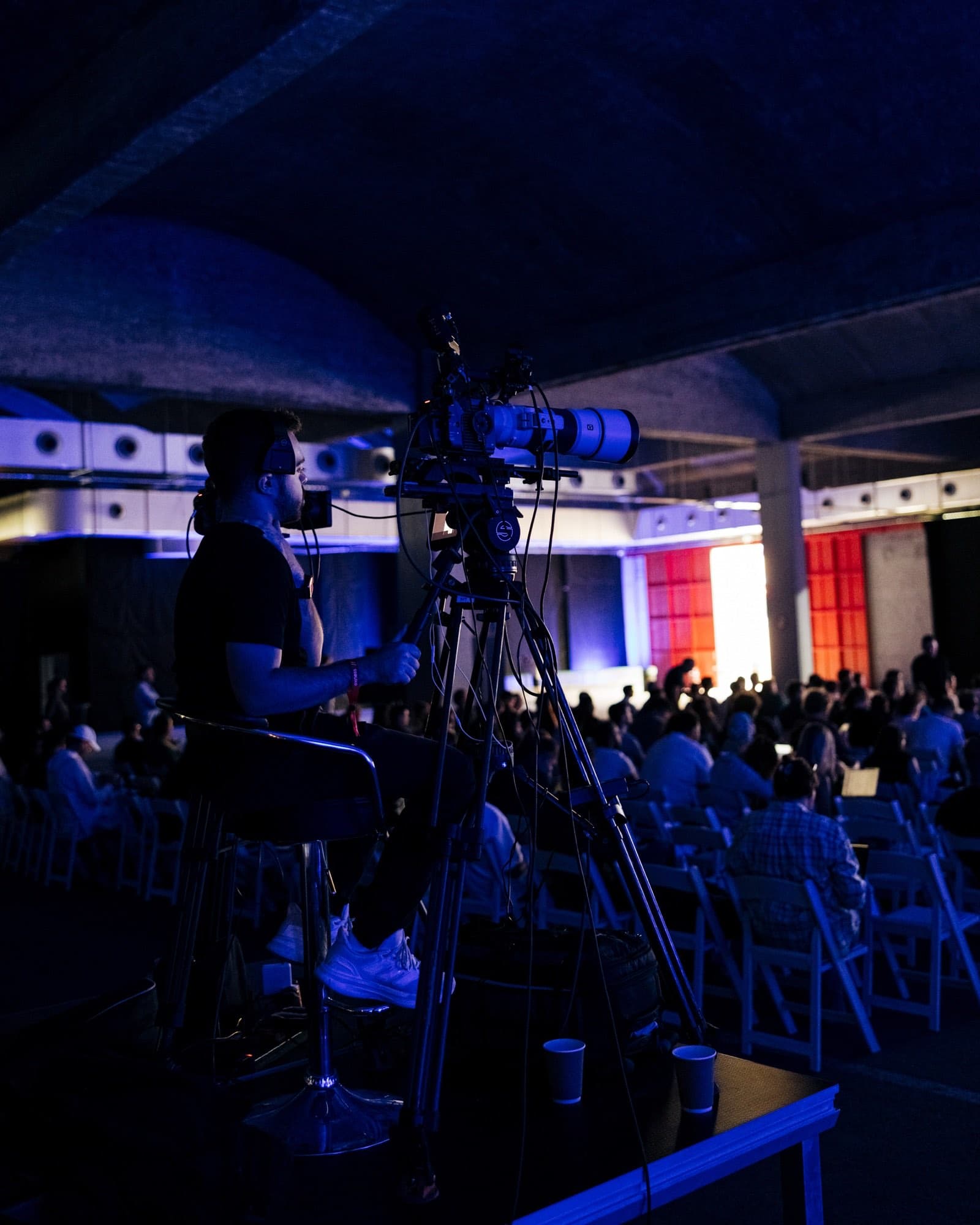 Backlight Media broadcast camera covering the Exness Week stage in a vaulted, purple-lit venue in Cyprus, part of the hybrid livestream linking Cyprus and Kuala Lumpur